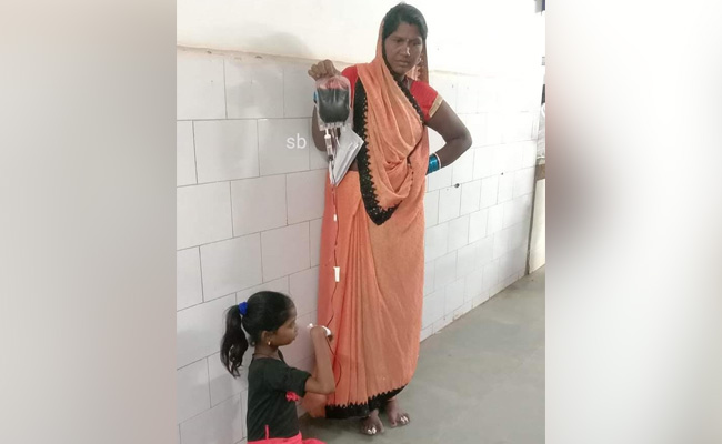 Woman Holds Blood Bag For Transfusion As Daughter Sits On Hospital Floor