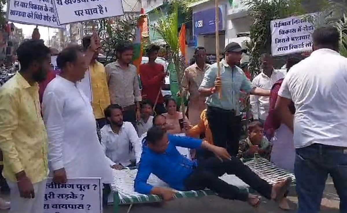 खंडवा में कांग्रेस का अनोखा प्रदर्शन, सड़क पर खटिया लगाकर लेटे, गड्ढों में पौधे लगाकर बनाया बगीचा