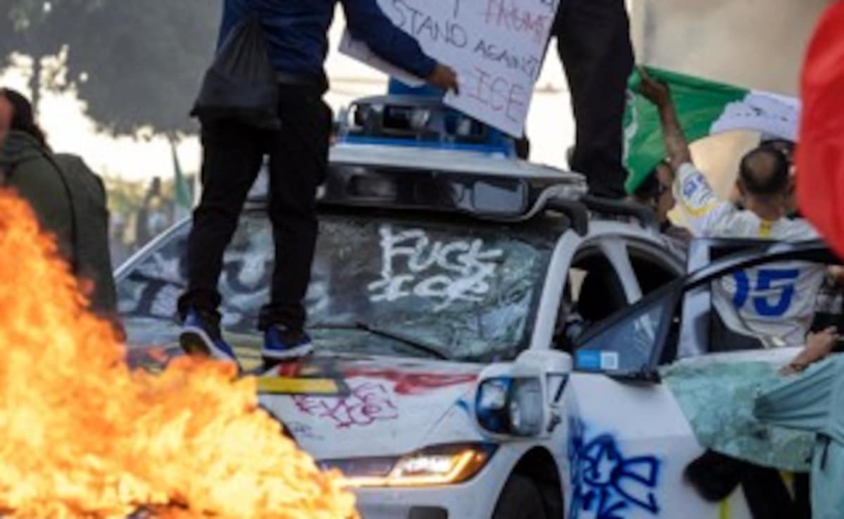 Demonstrators wave flags from atop a wrecked car, standing beside burning Waymo vehicles, as protesters clash with law enforcement in the streets surrounding the federal building during a protest following federal immigration operations in Los Angeles (Source: AFP) Demonstrators wave flags from atop a wrecked car, standing beside burning Waymo vehicles, as protesters clash with law enforcement in the streets surrounding the federal building during a protest following federal immigration operations in Los Angeles (Source: AFP)