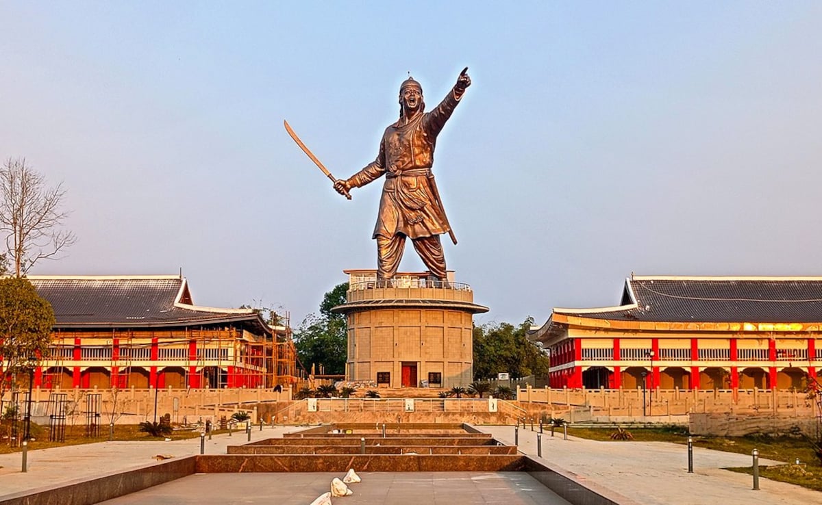 A grand statue of Ahom general Lachit Borphukan in Jorhat, Assam, standing with a raised sword amid traditional Assamese-style buildings under a clear sky.A grand statue of Ahom general Lachit Borphukan in Jorhat, Assam, standing with a raised sword amid traditional Assamese-style buildings under a clear sky.