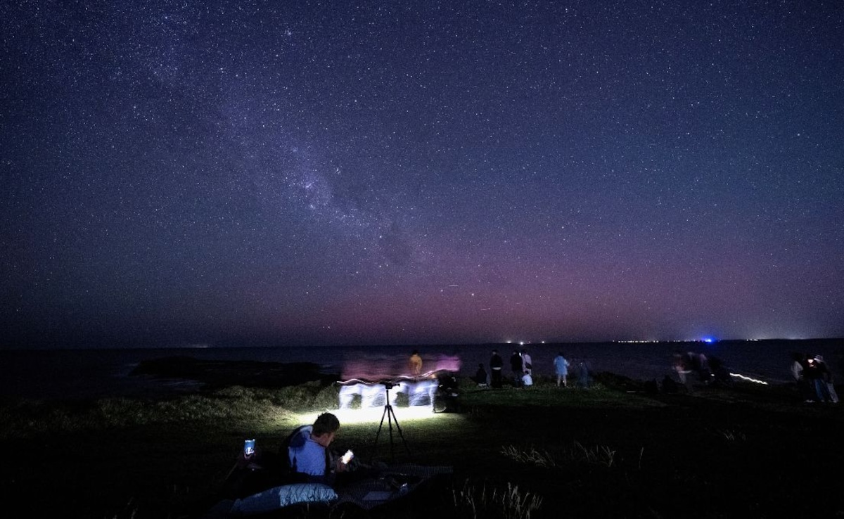 Star gazers gather to watch the Aurora Australis, also known as the Southern Lights, illuminating the night sky at Gerroa Headland in Kiama, around 133 kilometres south of Sydney, on November 13, 2025.