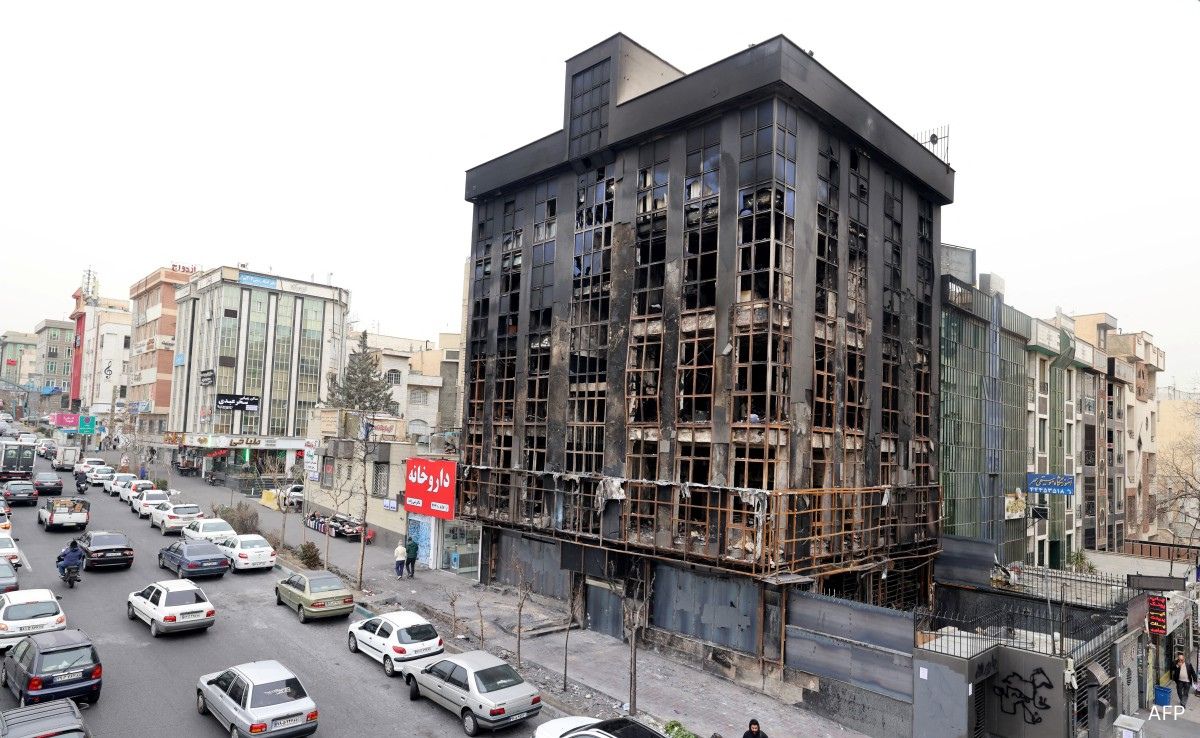 People walk past a burnt out building destroyed during public protests in Tehran