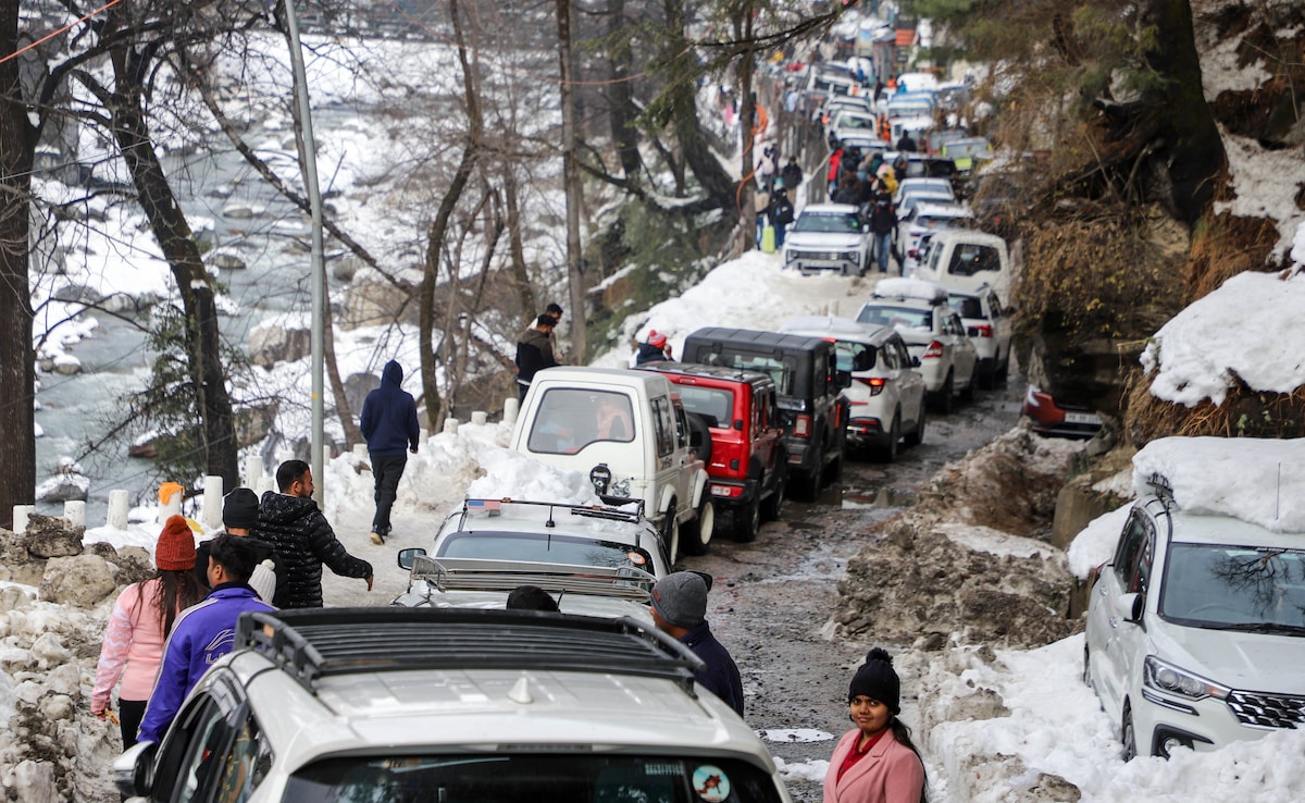 Tourists walk along a snow-covered road as vehicles remain stranded amid traffic congestion on the Manali highway