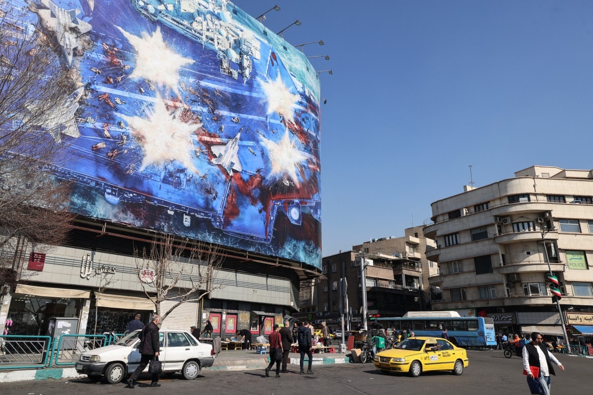 Iranians walk past an anti-US billboard installed on a building on Enqelab Square in Tehran (AFP)