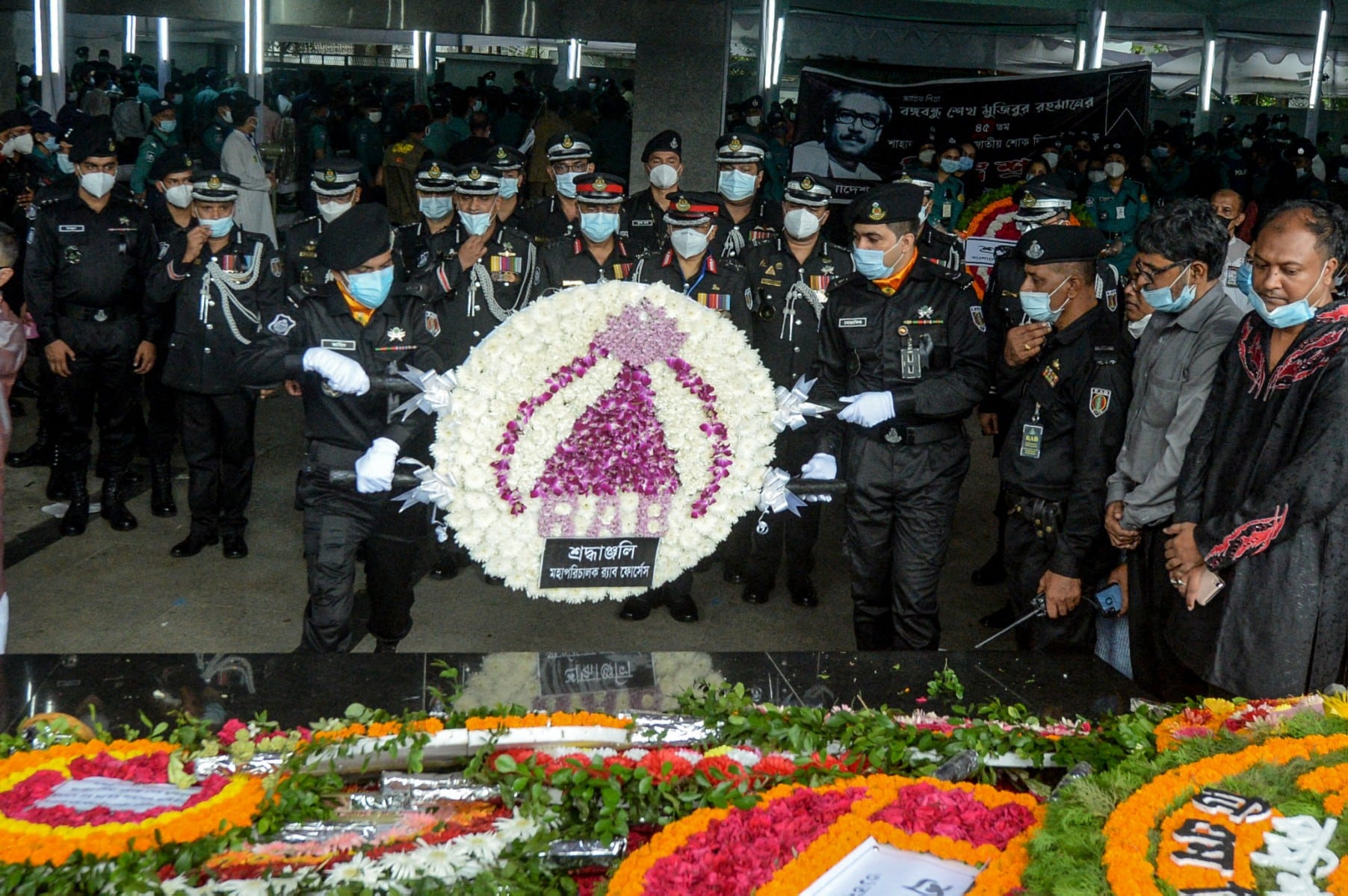 Ambtenaren van het Rapid Action Battalion plaatsen een bloemenkrans bij een muurschildering gewijd aan de eerste president en vader van de natie van Bangladesh, sjeik Mujibur Rahman, tijdens de Nationale Rouwdag in Dhaka op 15 augustus 2020.