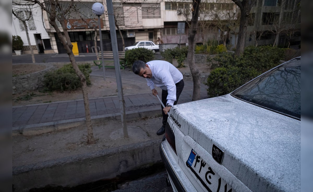A man cleaning his car covered with oil-soot residue in Tehran. (Getty)