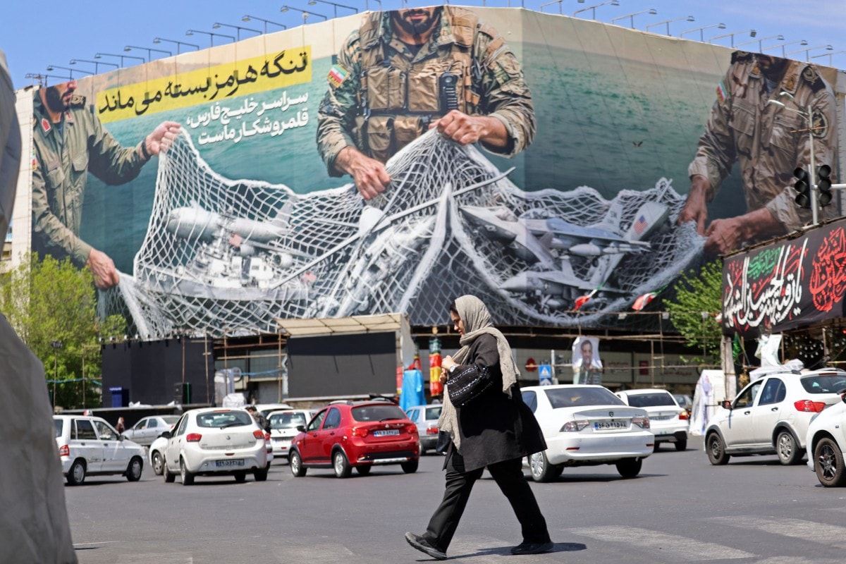 A woman walks past a giant billboard reading The Strait of Hormuz remains closed at the Revolution Square in Tehran on April 12, 2026.