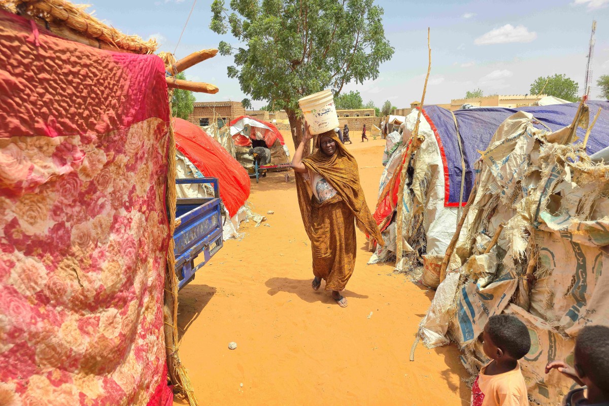 A Sudanese woman walks as she carries a plastic canister in al-Rahmaniyah camp for displaced people, near the city of El-Obeid in the southern Kordofan region, on June 25, 2026. The Sudanese city of El-Obeid is only "weeks" away from a humanitarian disaster unless aid is urgently allowed in, a UN official told AFP on June 23, as fears grow of an imminent paramilitary offensive. A strategic hub in the southern Kordofan region, the city has been encircled for months by the Rapid Support Forces, the paramilitary group that has been fighting Sudans army since April 2023.