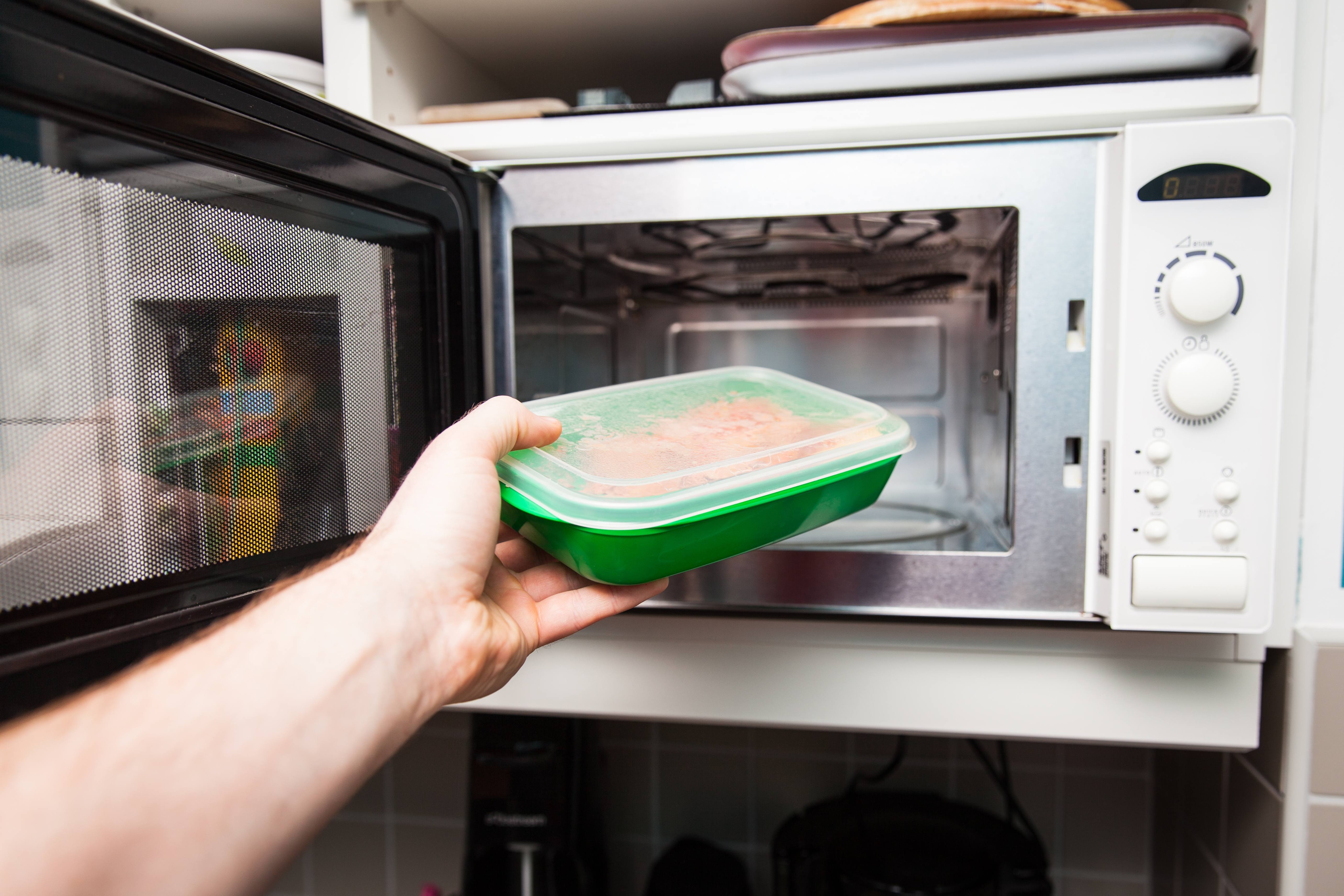 A person places a plastic food container inside a microwave for reheating. A person places a plastic food container inside a microwave for reheating.