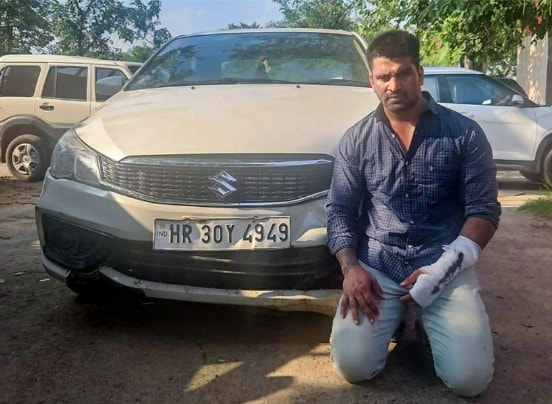 Kalyan Bainsla, with his heavily bandaged hand, kneels beside his vehicle in police custody following his arrest Kalyan Bainsla, with his heavily bandaged hand, kneels beside his vehicle in police custody following his arrest