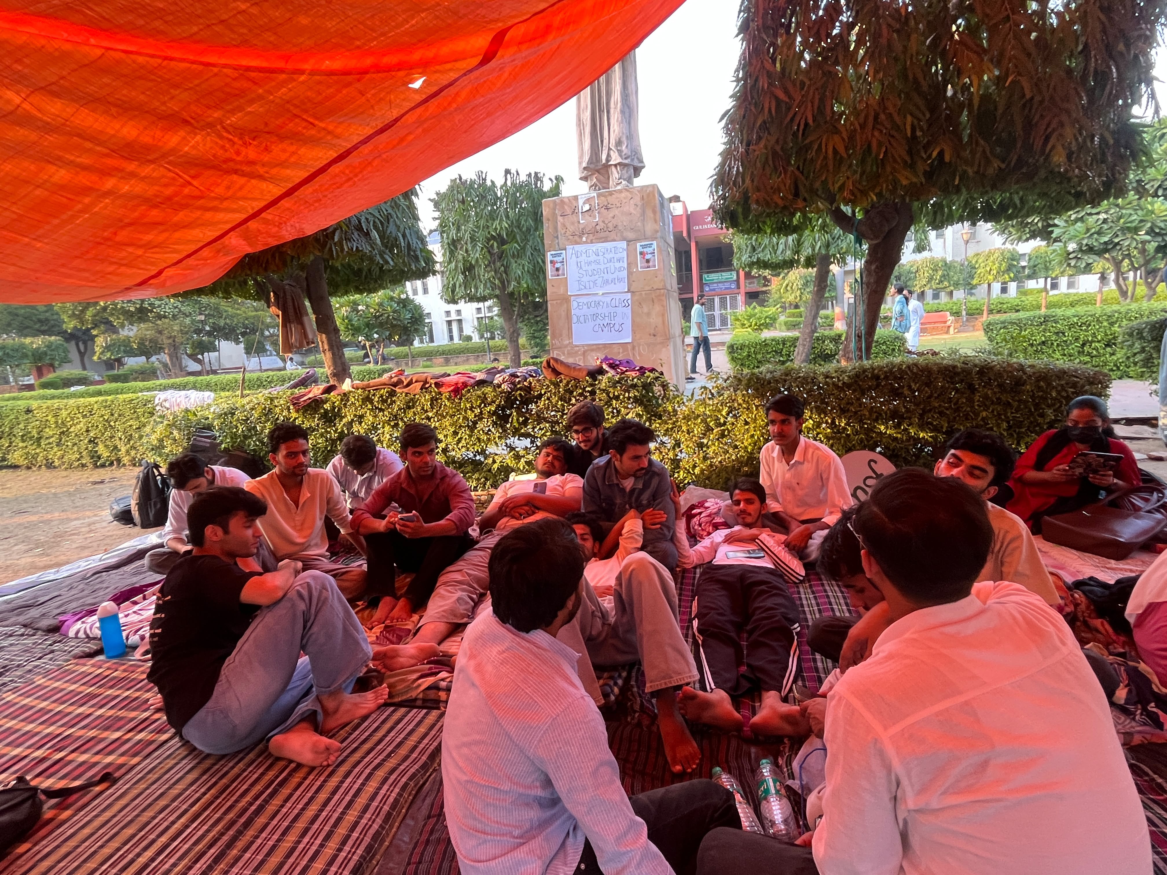 तिरपाल के नीचे बैठे प्रदर्शनकारी छात्र