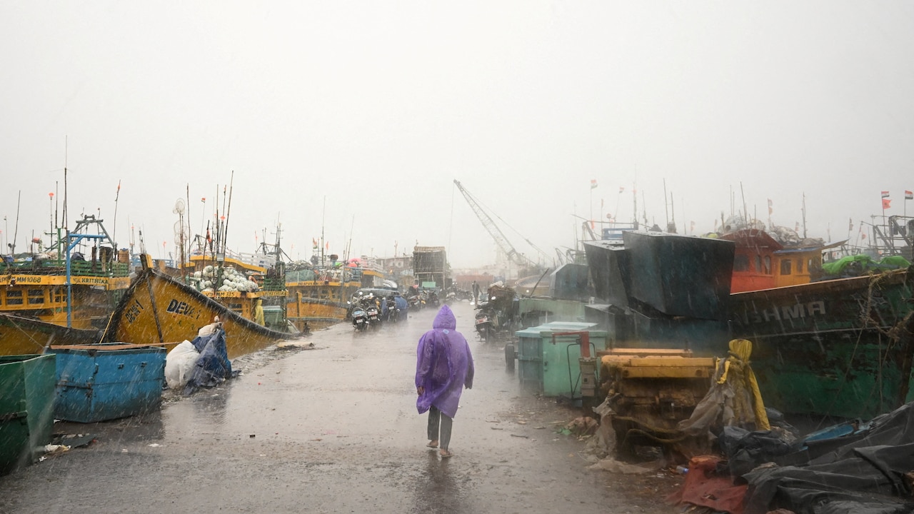 A man walks past docked boats along the harbour amid rain and gusty winds as Cyclone Arnab approaches, in Visakhapatnam on October 27