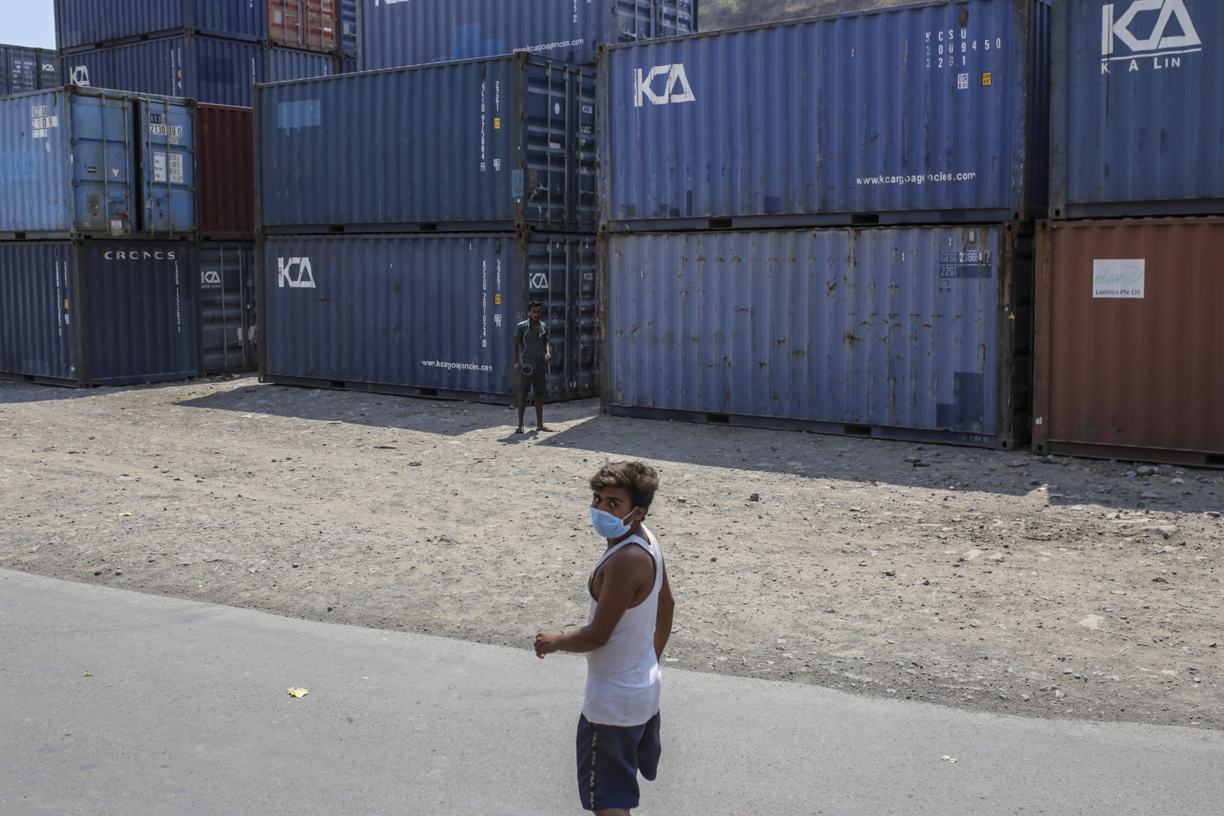 A man wearing a protective mask walks past shipping containers at the Jawaharlal Nehru Port, operated by Jawaharlal Nehru Port Trust (JNPT), in Navi Mumbai, Maharashtra, India. (Photographer: Dhiraj Singh/Bloomberg)