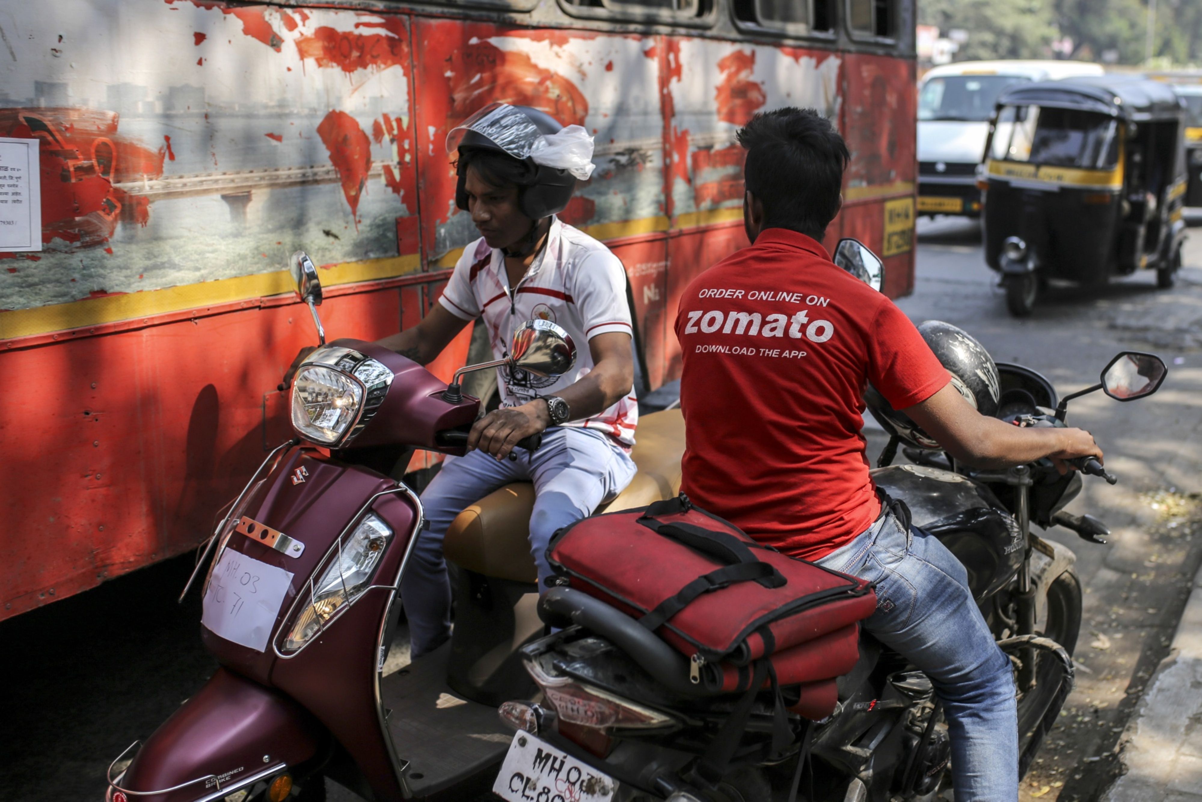 A food delivery rider for Zomato Media Pvt., right, rides a motorcycle in Mumbai, India. (Photographer: Dhiraj Singh/Bloomberg)