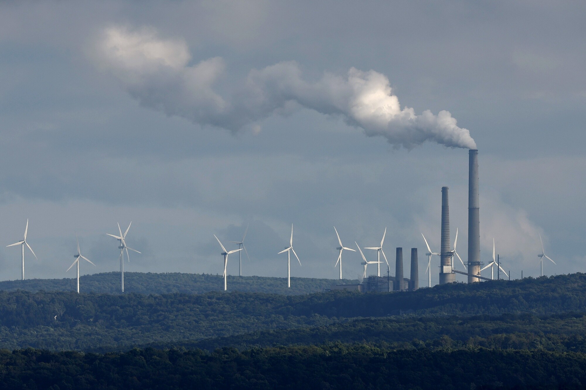 Wind turbines stand behind a power station in Mount Storm, West Virginia. Photographer: Chip Somodevilla/Getty Images